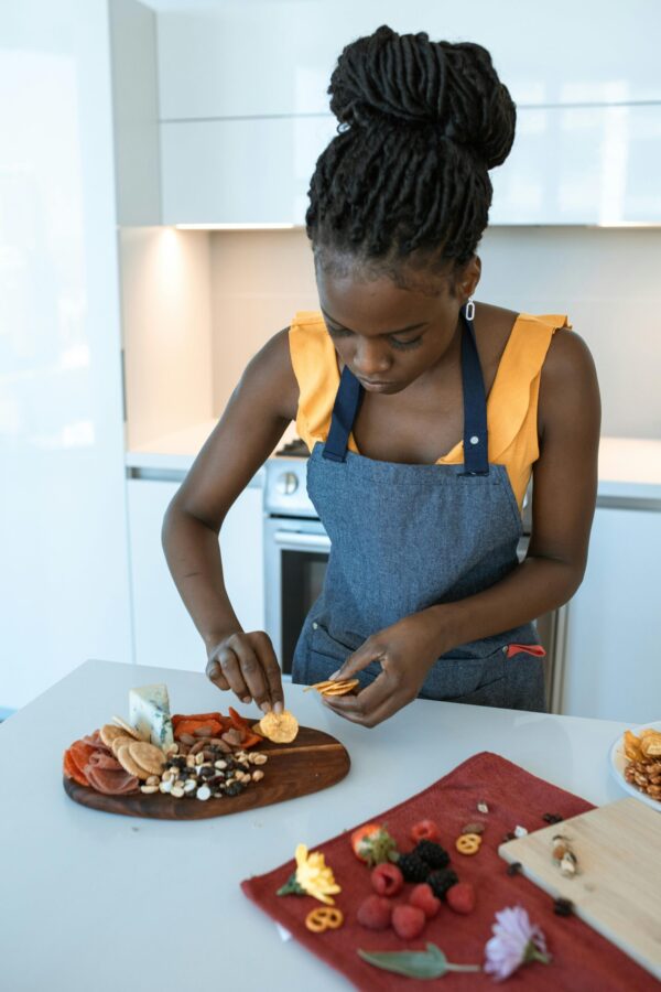 Woman in apron arranging a charcuterie board in a contemporary kitchen setting.